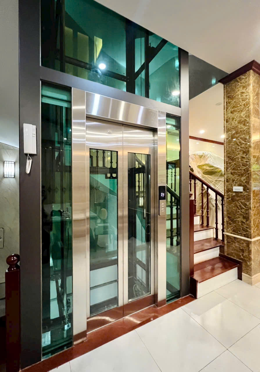 Thang máy gia đình vách kính khung inox lắp cạnh cầu thang trong nhà sang trọng